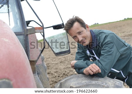Smiling handsome farmer leaning on tractor
