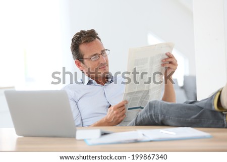 Man reading newspaper with stretched legs over table