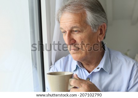 Senior man looking by window, holding cup of tea