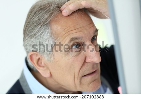 Senior man looking at hair loss in mirror