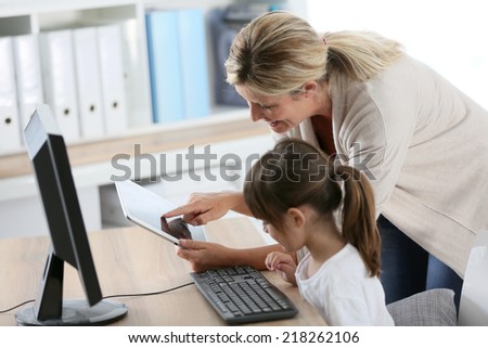 Teacher with little girl in class using computer and tablet