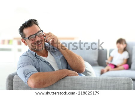 Man in sofa talking on phone, girl in background