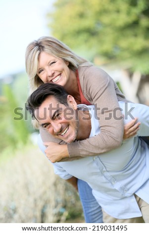 Cheerful mature man giving piggyback ride to woman