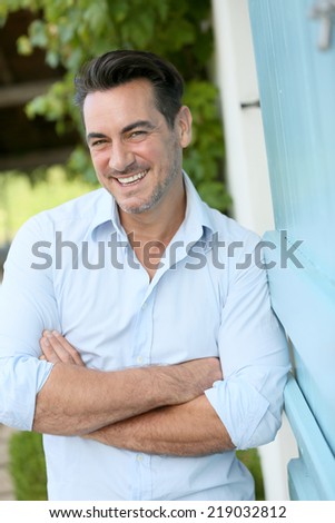 Smiling 40-year-old man leaning on home wall