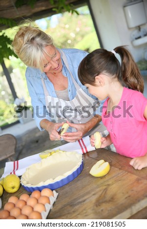 Grandmother cooking apple pie with little girl