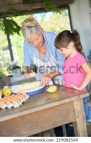 Grandmother cooking apple pie with little girl