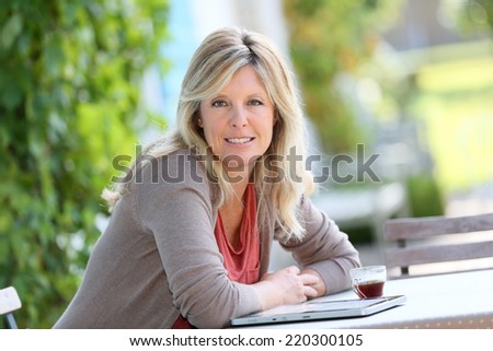 Mature woman relaxing with tablet and coffee in garden