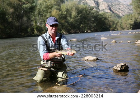 Fly fisherman catching a fario trout in river