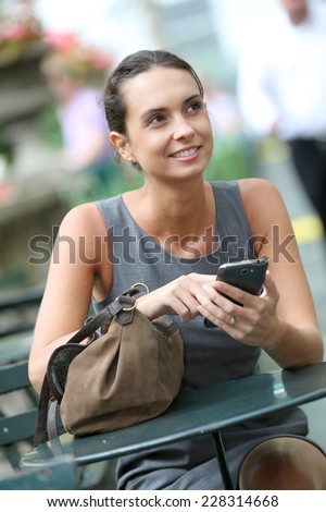 Businesswoman with smartphone in park, waiting for someone