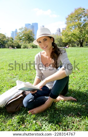 Cheerful woman in Central Park reading New York city guide