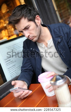 Man sitting at coffee shop, checking email on smartphone
