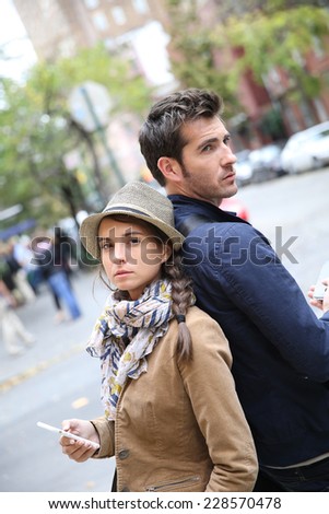 Couple standing back to back in street, using smartphone