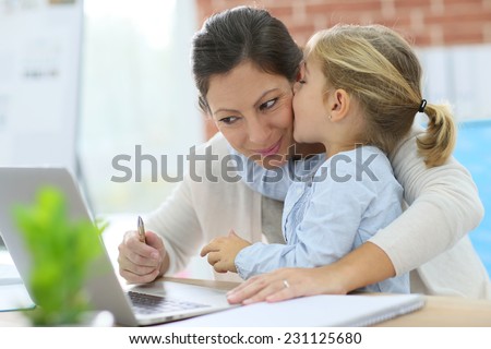 Little girl giving kiss to her mom while working from home