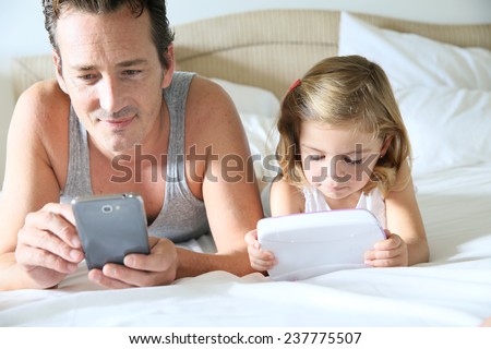 Man with smartphone and daughter playing with child\'s tablet