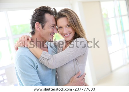 Cheerful 40-year-old couple embracing in home living-room