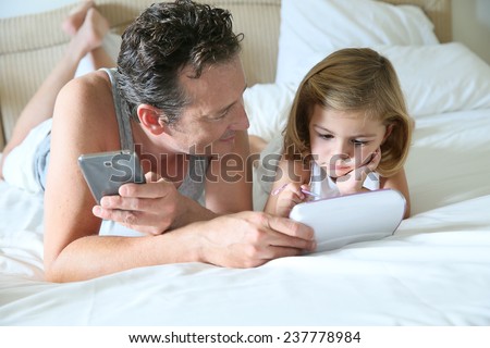 Man with smartphone and daughter playing with child\'s tablet