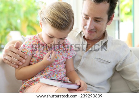 Man with daughter playing with child\'s tablet