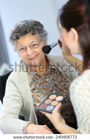Home carer helping elderly woman to put makeup on