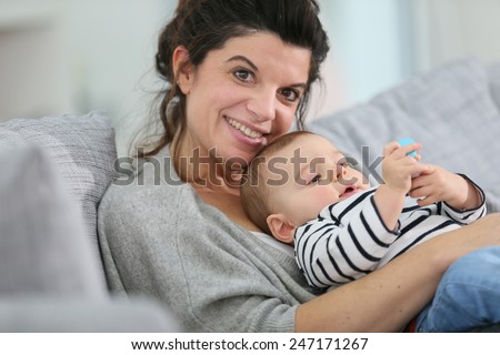 Cheerful mother cuddling in sofa with baby son