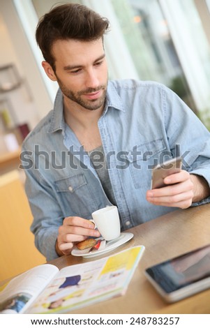 Man in coffee shop sending message with smartphone