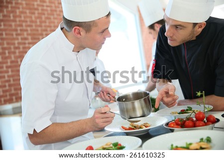 Chef with young cook in kitchen preparing dish