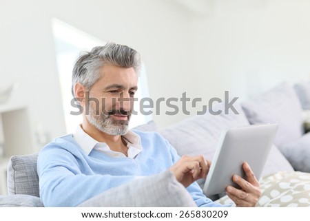Mature handsome man websurfing on tablet at home