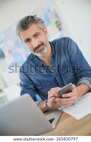 Teacher using laptop and smartphone in school office