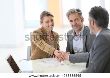 Couple in bank office shaking hand to financial adviser