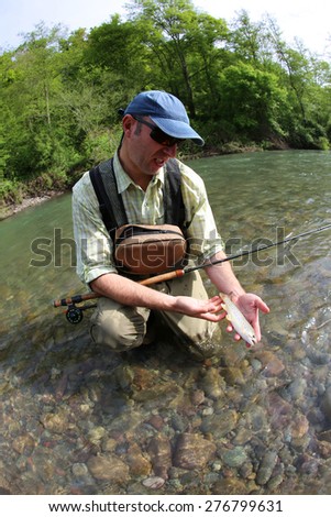 Fisherman catching brown trout with fishing line in river