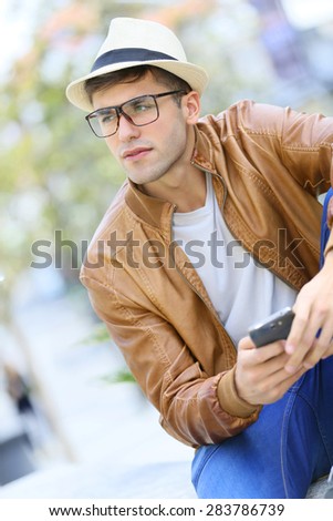 Hipster guy using smartphone sitting on public bench