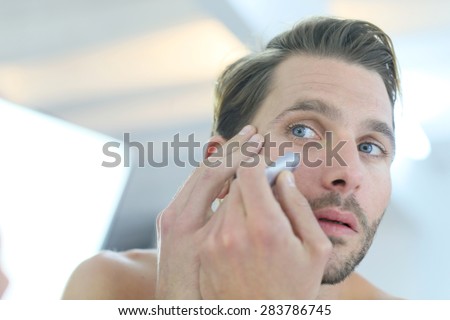 Man in front of mirror using cosmetic cream