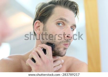 Man in front of mirror using electronic shaver