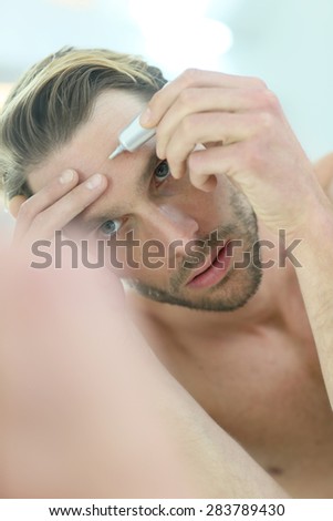 Man in front of mirror using cosmetic cream