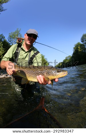 Closeup of fly-fisherman holding brown truit in river