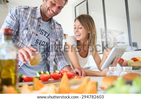 Cheerful couple in kitchen cooking dinner, using tablet