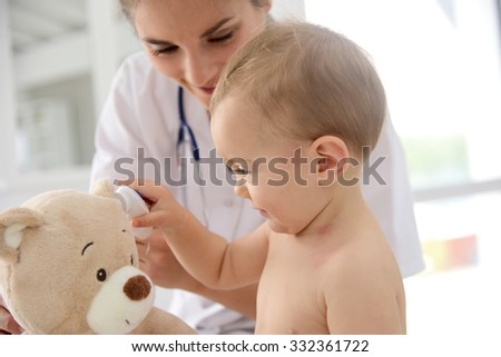 Baby in doctor\'s office playing with stethoscope and teddy bear