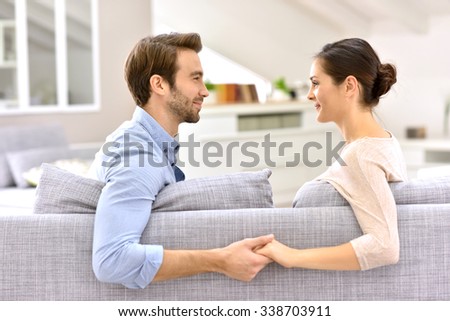 Man and woman in sofa, facing each other and holding hands