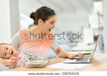 Busy mother trying to work and feed kid at the same time