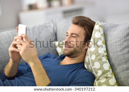 Man relaxing in sofa and playing with smartphone