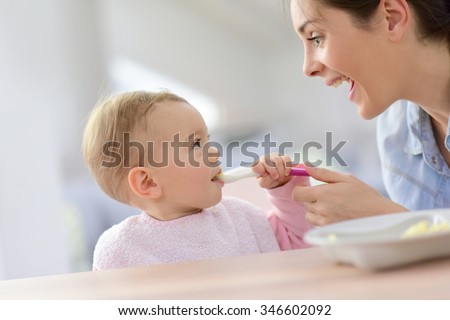 Baby girl eating lunch with help of her mommy