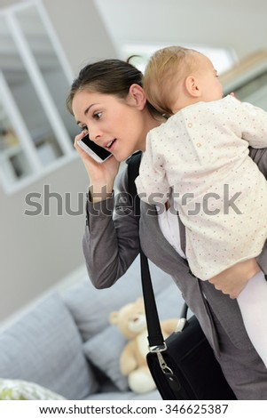 Busy businesswoman talking on phone and holding baby in arms