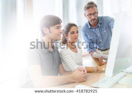 Teacher with group of students in class working on desktop