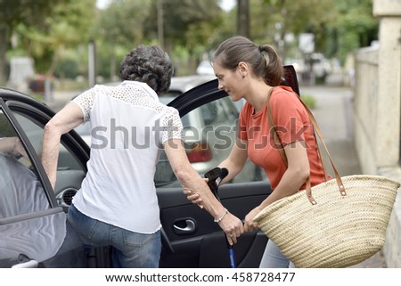 Young carer helping senior woman getting in car