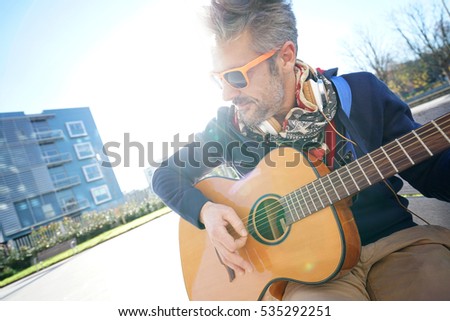 Mature trendy guy playing the guitar in the street