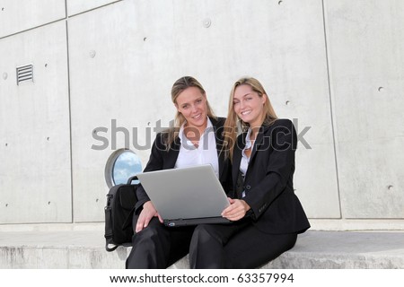 Women working on laptop computer in front of concrete building