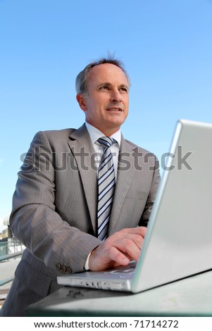Smiling businessman working outside with laptop computer