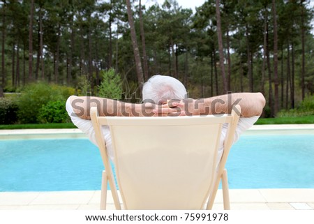 Senior man relaxing in deck chair by a pool