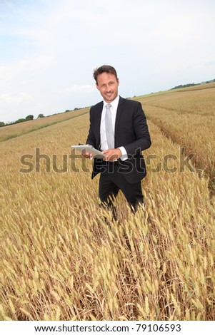 Businessman with electronic tablet standing in wheat field
