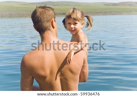 A man stands in water with a little girl in his arms
