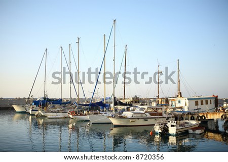 sunlit yachts and boats reflected on water at marina with clean blue sky as background
